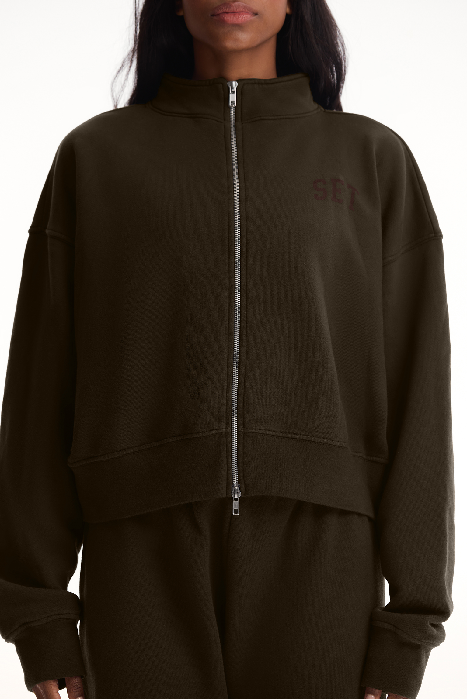 Person wearing a dark brown zip-up hoodie with a logo on a white background