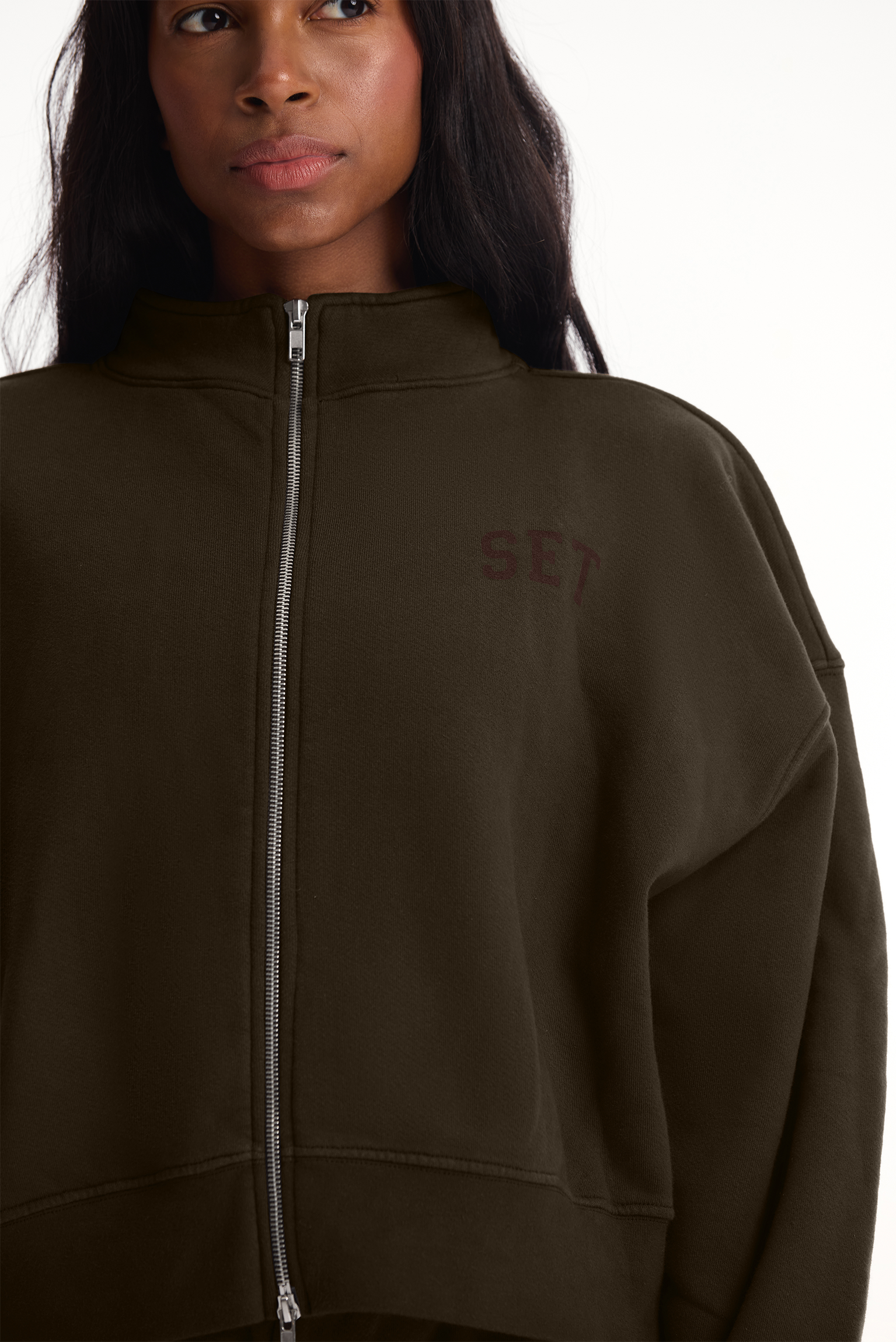 Person wearing a brown zip-up hoodie with 'SET branding on a white background