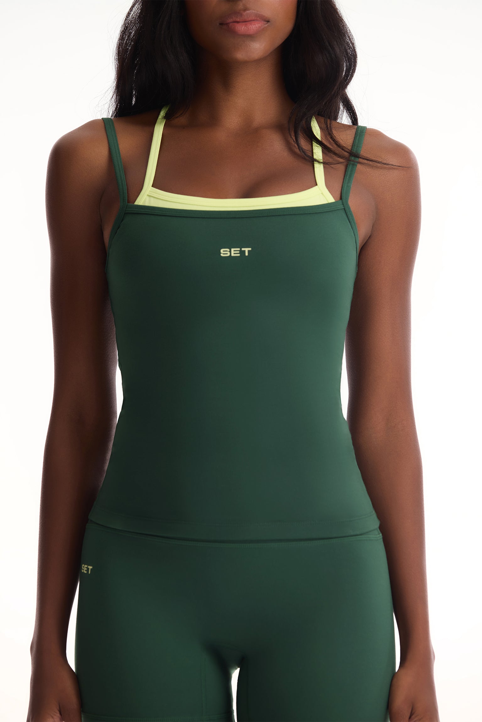 Green athletic tank top with yellow straps worn by a model on a white background