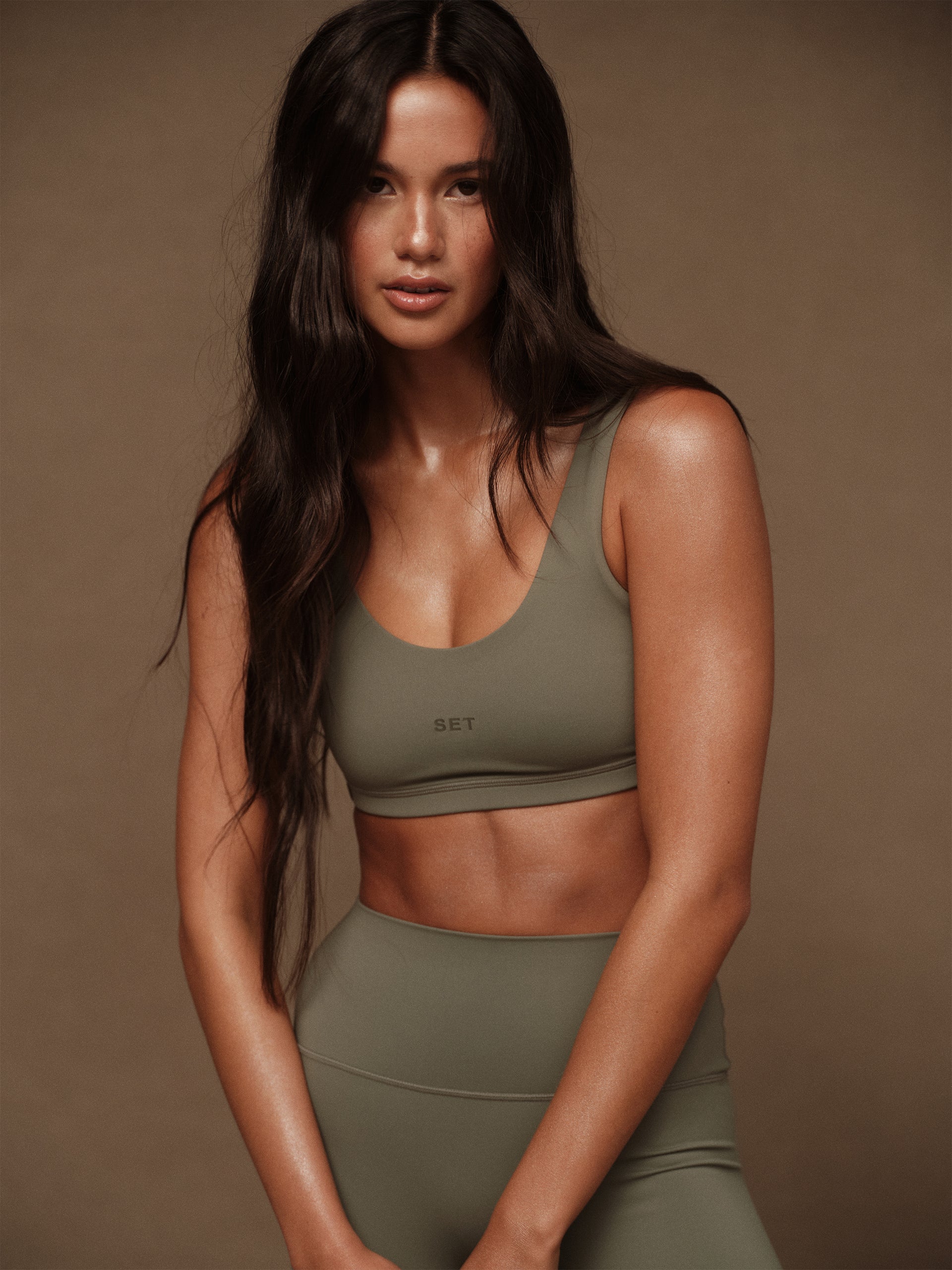 Woman wearing a green sports bra and leggings on a brown background