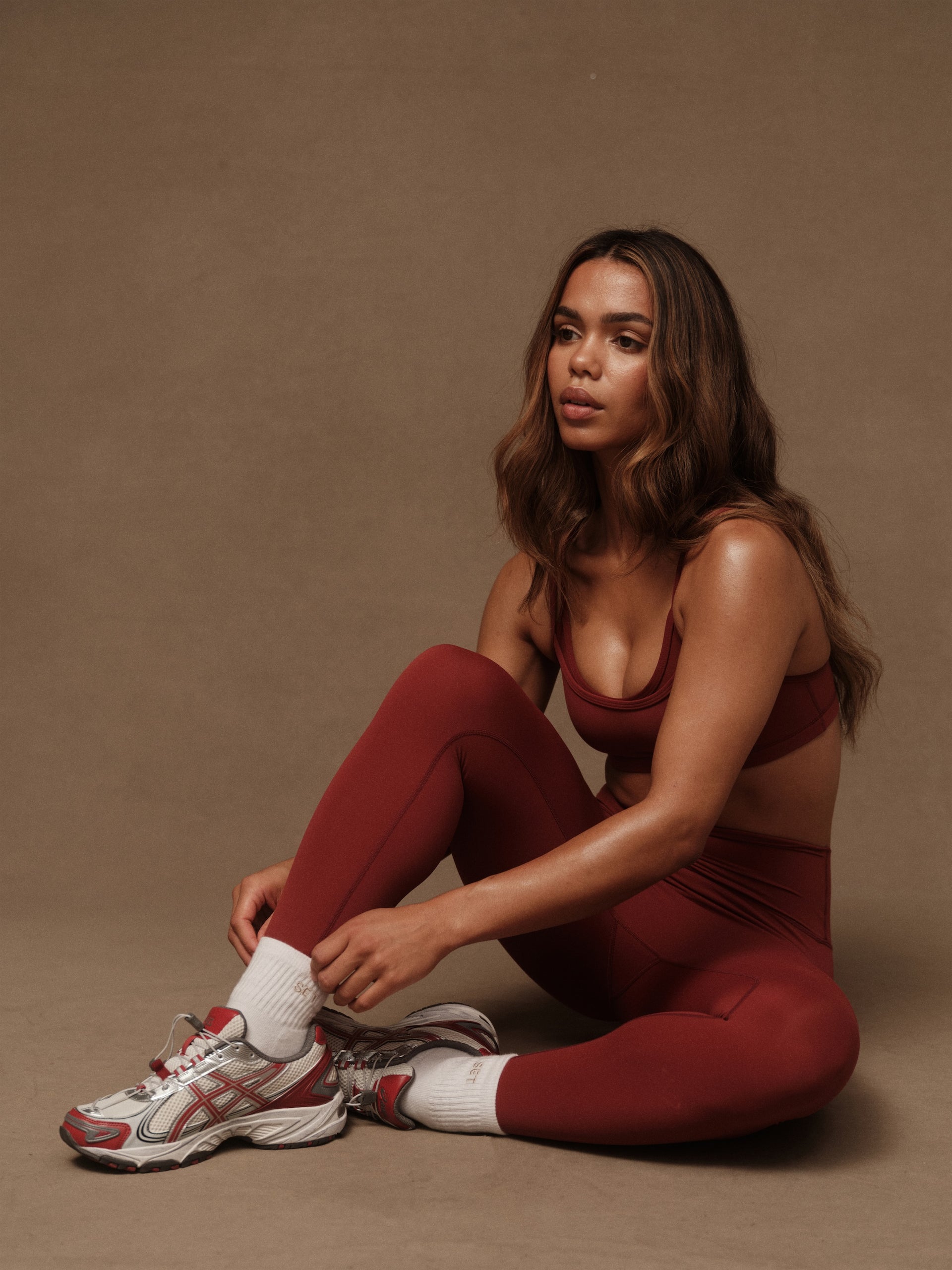 Woman in red athletic wear sitting on a brown background