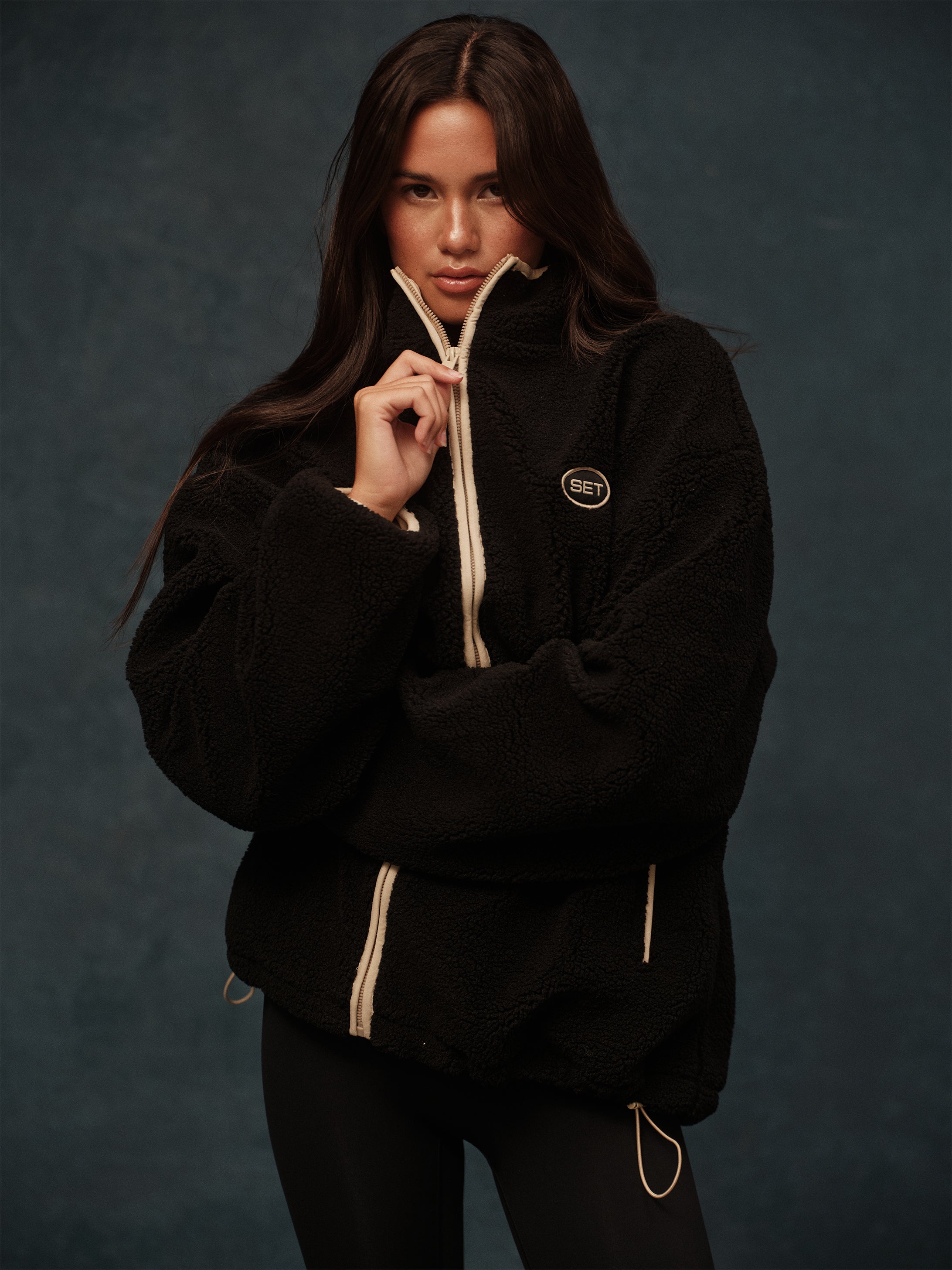 Person wearing a black jacket with a brand logo on a dark background