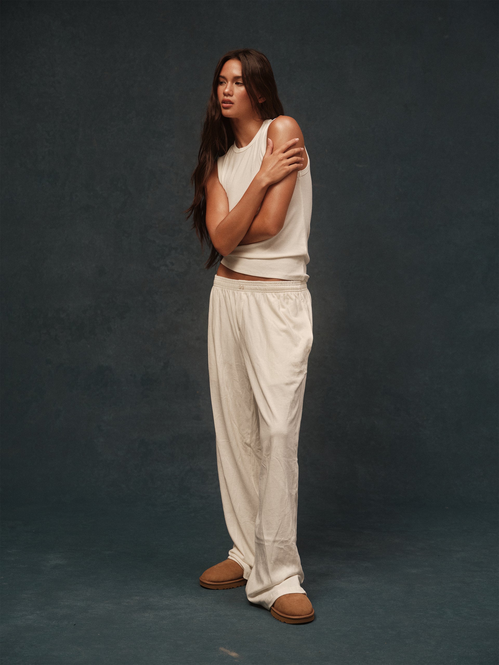 Woman wearing a white sleeveless top and pants against a dark background