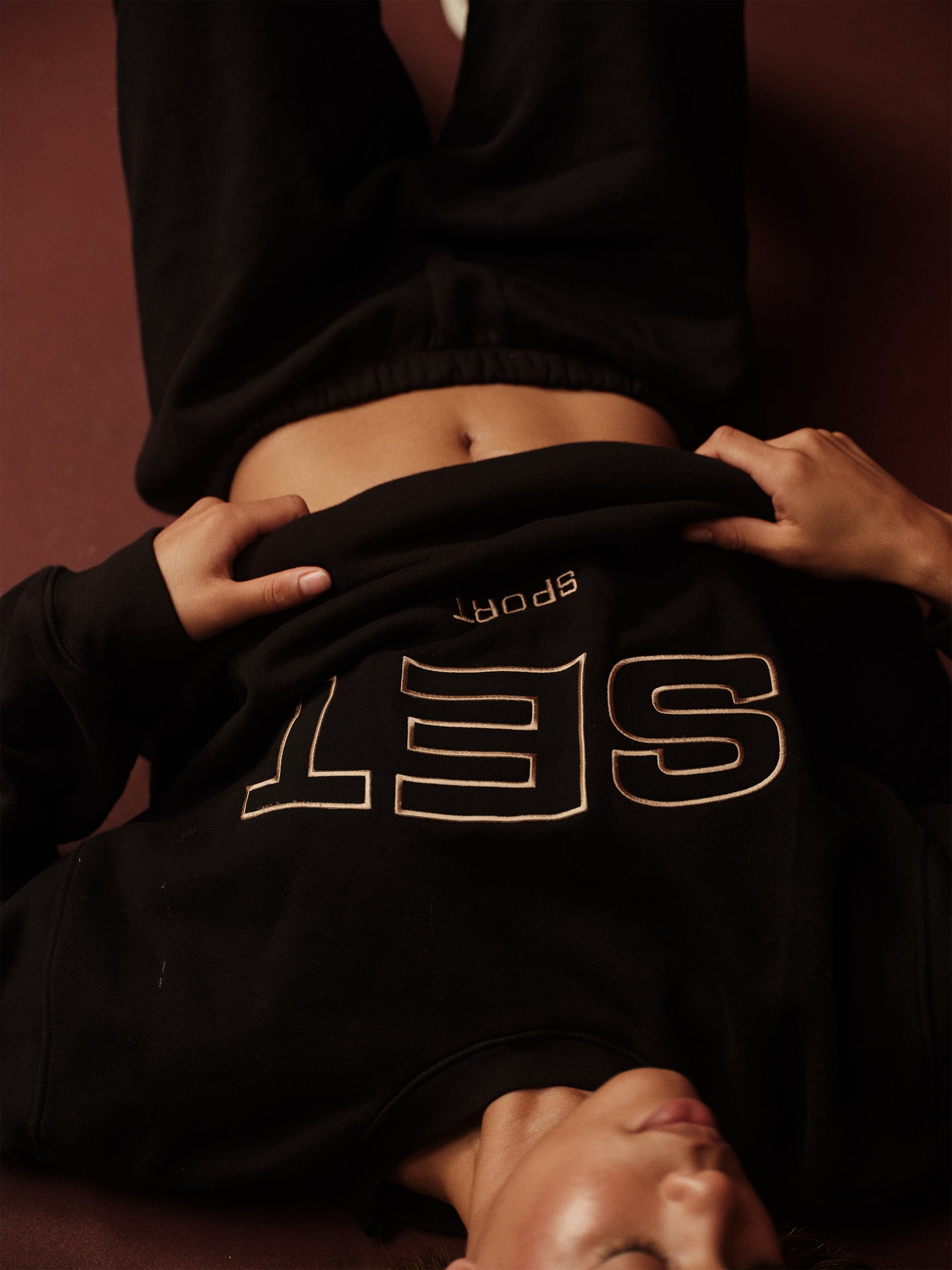 Person wearing a black hoodie with 'SET' logo, sitting on a brown surface.