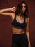 Woman in black sports bra and leggings posing against a brown background