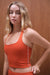 Woman wearing an orange tank top against a wooden background <model-info>Grace wears a size XS and is 5'8", 25" waist, 32" bust.</model-info>