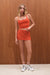 Woman wearing an orange outfit standing against a wooden wall.