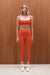 Woman wearing an orange athletic outfit standing against a wooden wall.