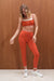 Woman wearing a red sports bra and leggings set against a wooden background