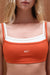 Orange sports bra with white straps and 'SET' logo on a beige background