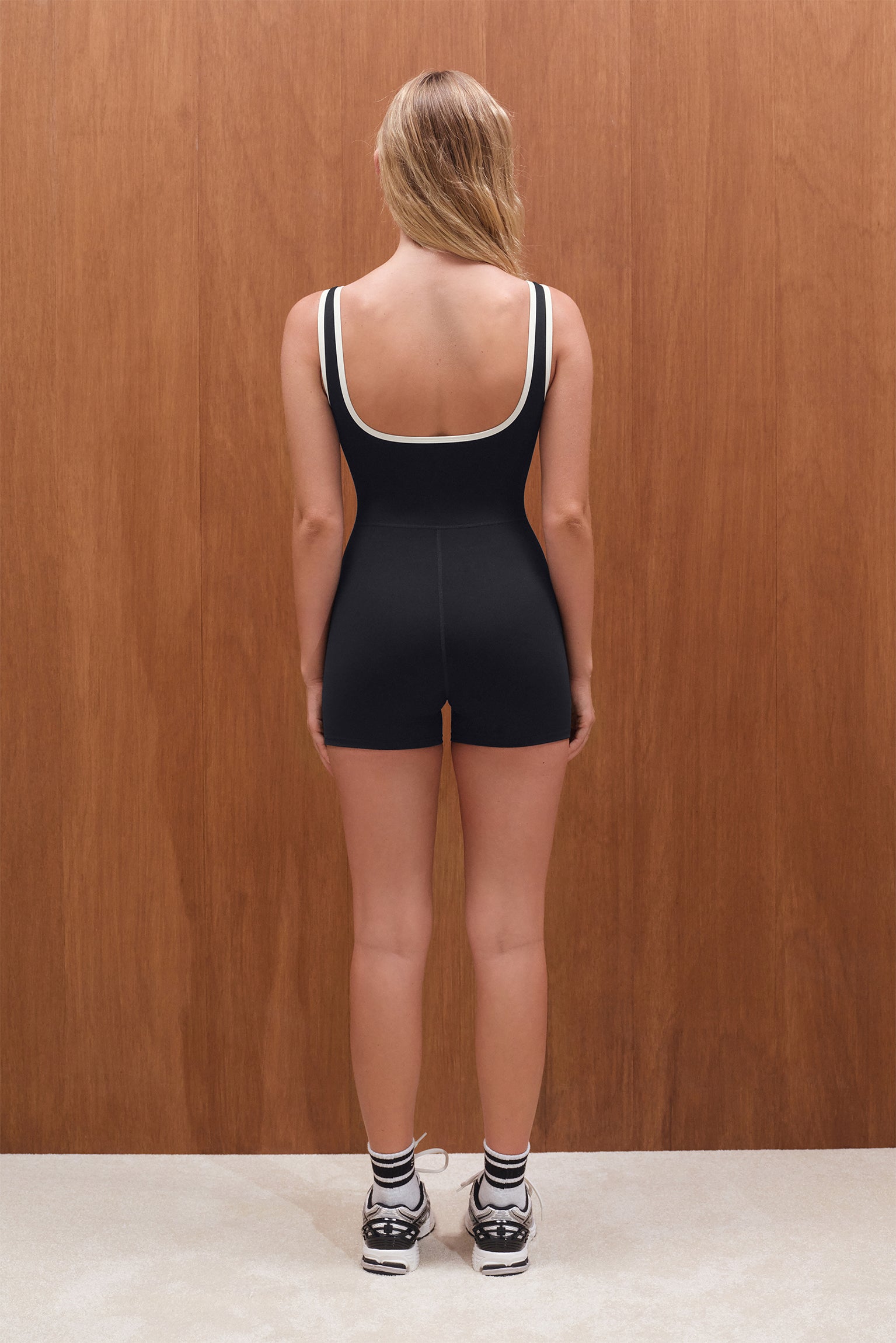 Person wearing a black unitard against a wooden wall