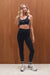 Woman wearing a black sports bra and leggings with white sneakers against a wooden background