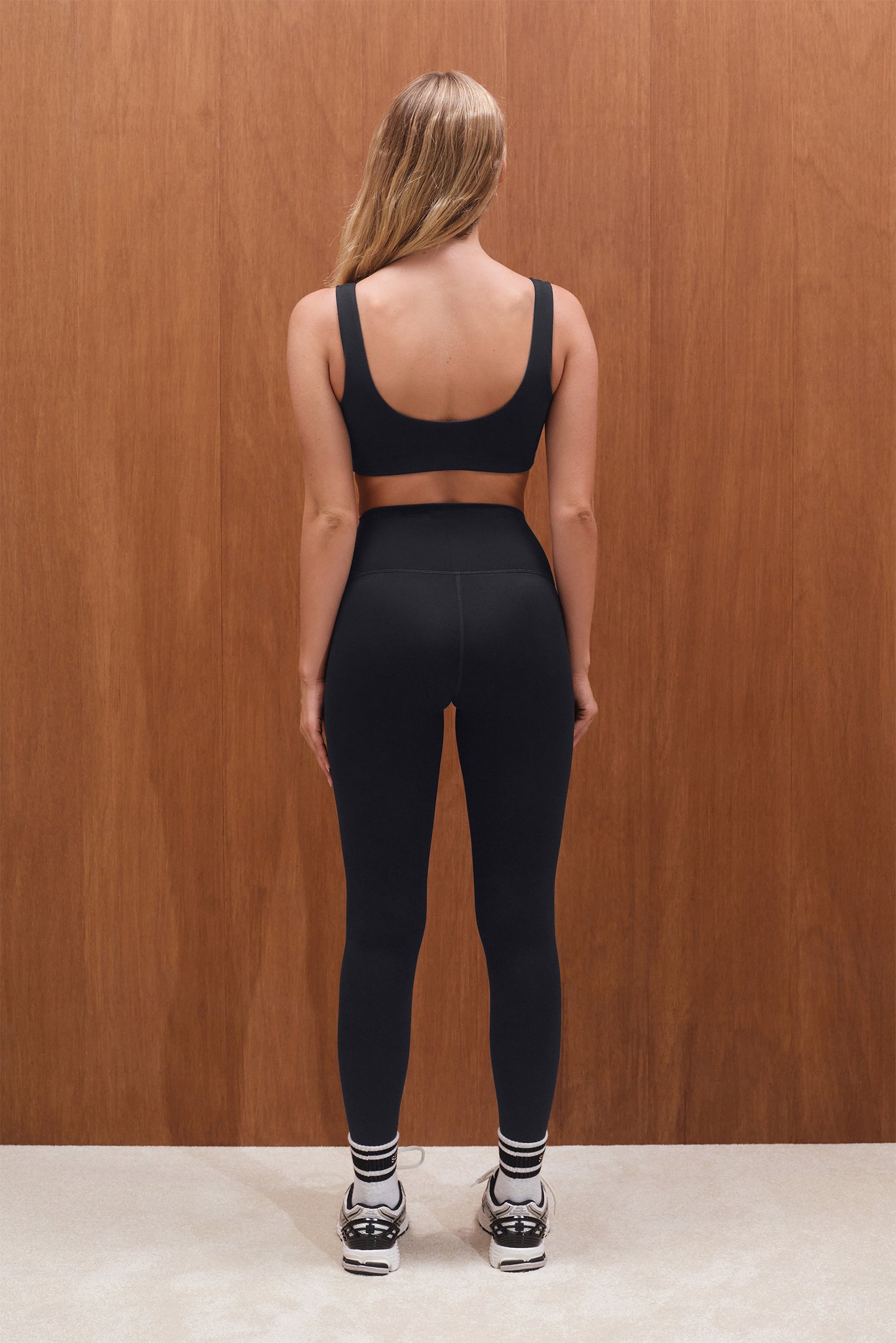 Person wearing a black sports bra and leggings set with a wooden background