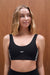 Woman wearing a black sports bra with 'SET' branding against a wooden background <model-info>Grace wears a size XS and is 5'8", 25" waist, 32" bust.</model-info>
