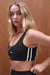 Woman wearing a black sports bra with white stripes against a wooden background