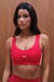 Woman wearing a red sports bra with 'SET' branding against a wooden background <model-info>Sydnee wears a size XS and is 5'8", 22” waist, 32BB bust.</model-info>