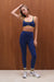Woman wearing a blue sports bra and leggings with yellow accents against a wooden background