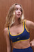 Woman wearing a blue sports bra with yellow trim against a wooden background