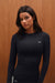 Woman wearing a black long-sleeve shirt with 'SET' logo against a wooden background <model-info>Sydnee wears a size XS and is 5'8", 22” waist, 32BB bust.</model-info>