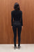 Person wearing a black outfit standing against a wooden wall.