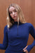 Woman wearing a blue long-sleeve top against a wooden background <model-info>Grace wears a size XS and is 5'8", 25" waist, 32" bust.</model-info>