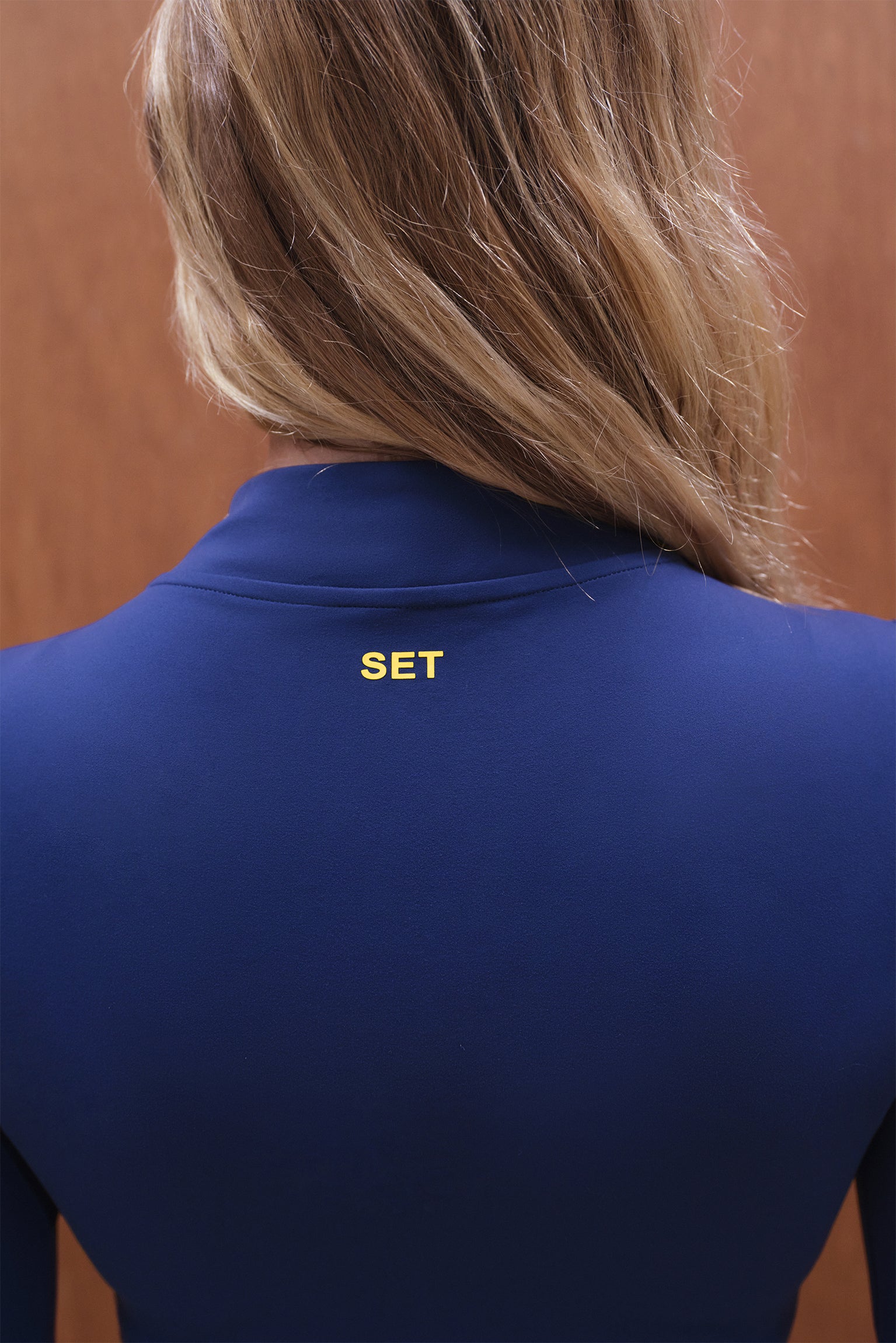 Blue jacket with 'SET' logo on the back, worn by a person with blonde hair.