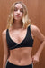 Woman wearing a black sports bra against a wooden background <model-info>Grace wears a size XS and is 5'8", 25" waist, 32" bust.</model-info>