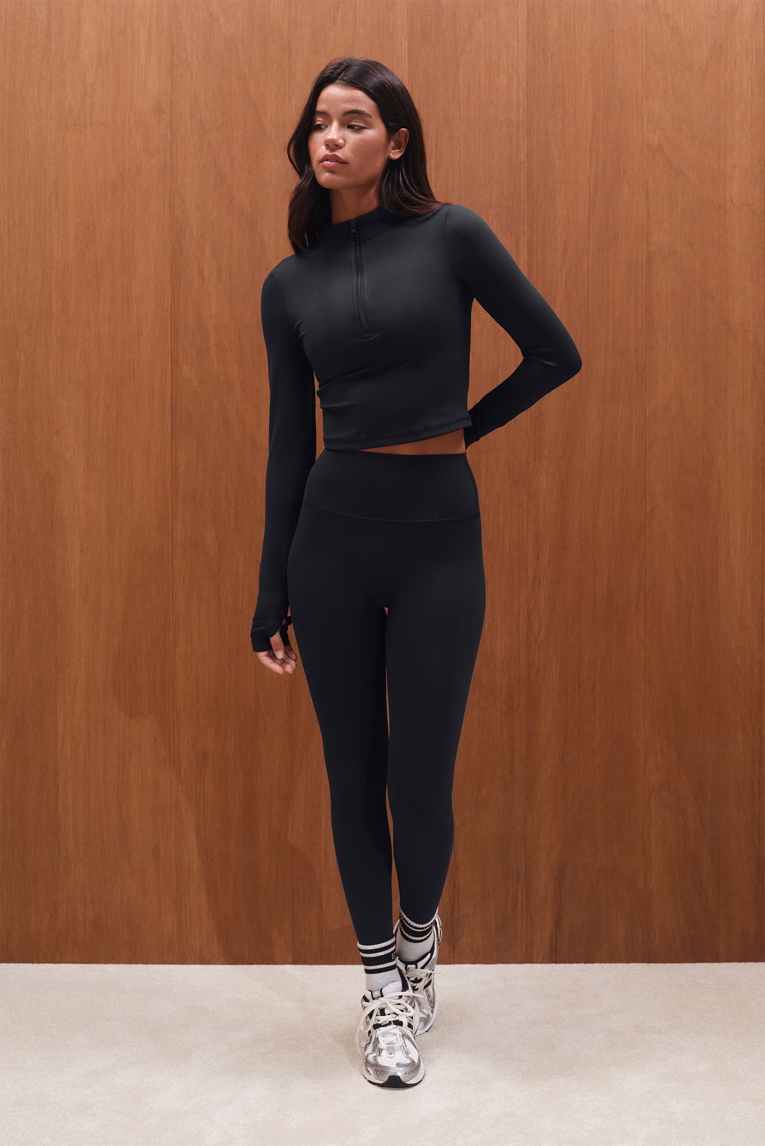 Woman wearing a black athletic outfit standing against a wooden wall.