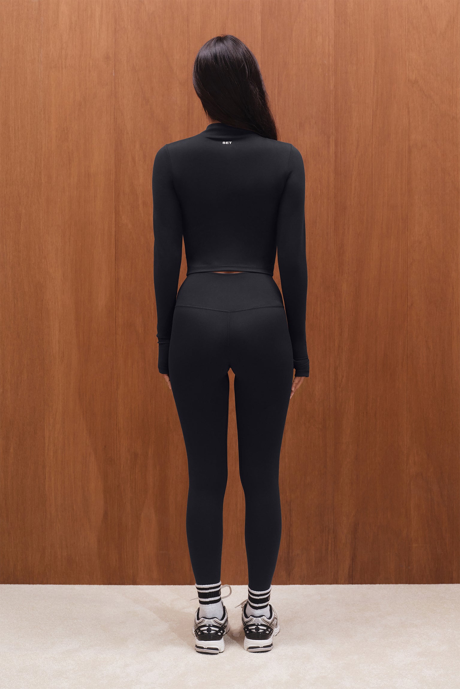 Person wearing a black outfit standing against a wooden wall.