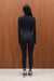 Person wearing a black outfit standing against a wooden wall.