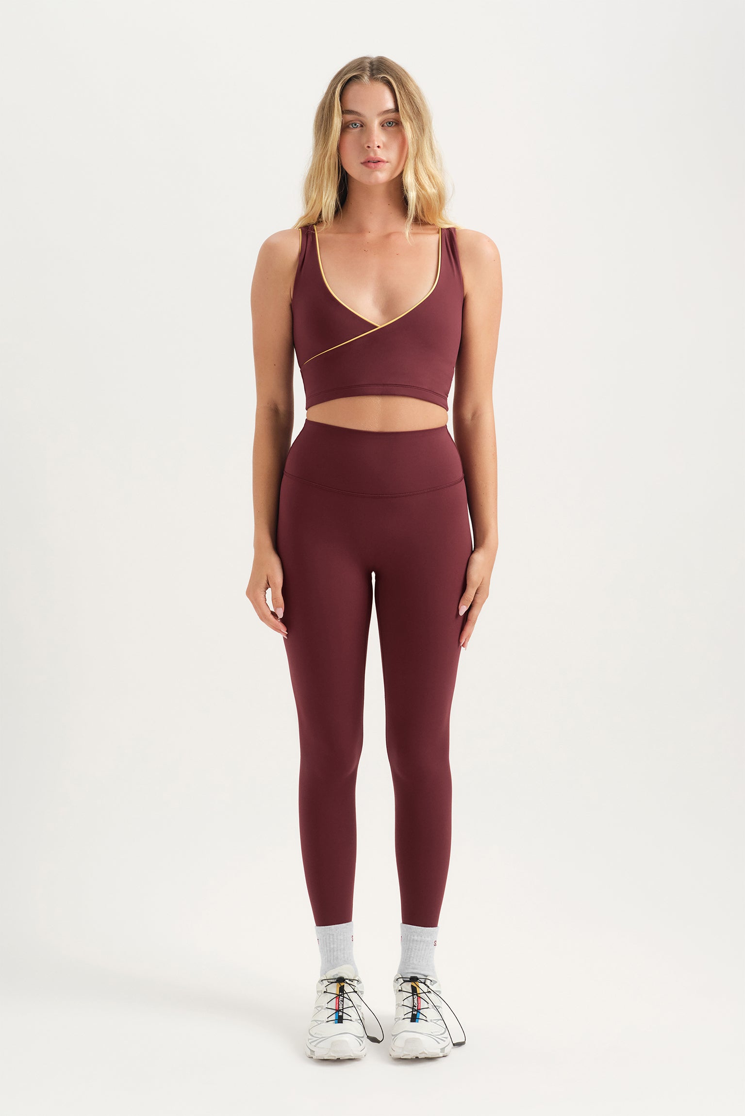 Woman wearing a maroon sports bra and leggings set on a white background