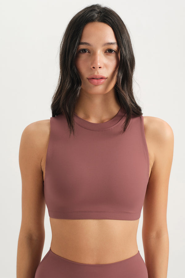 Woman wearing a mauve sports bra and leggings on a light gray background 
