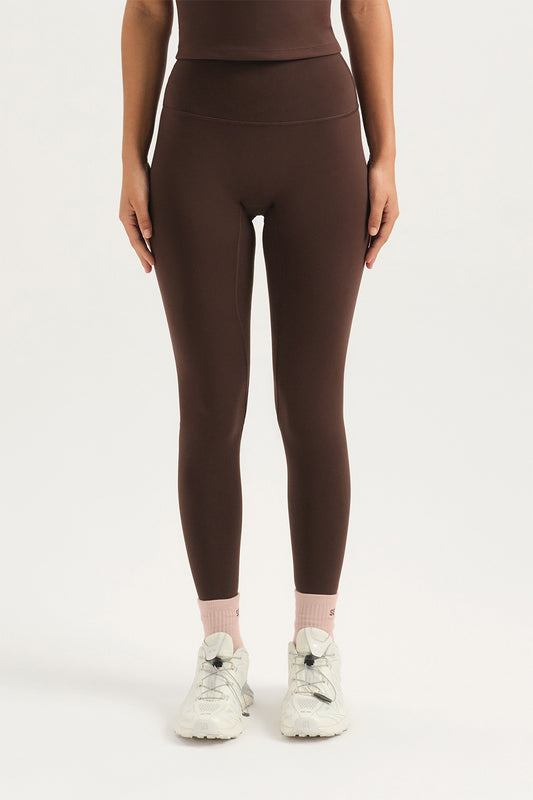 Person wearing brown leggings and white sneakers on a white background <model-info>Sydnee wears a size XS and is 5'8", 22” waist, 32BB bust.</model-info>