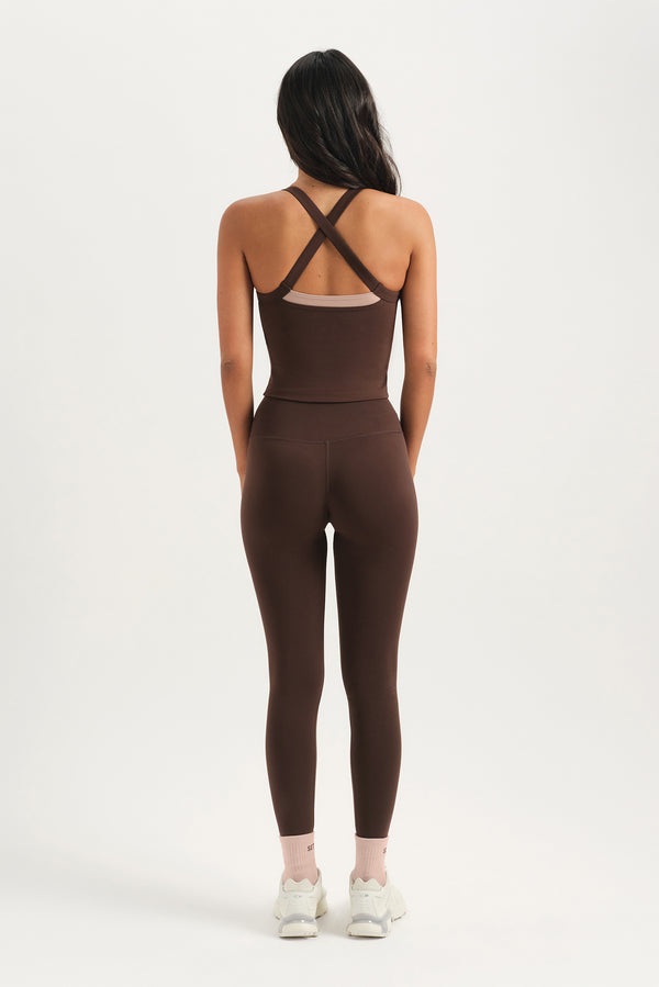 Person wearing a brown jumpsuit with criss-cross straps on a white background