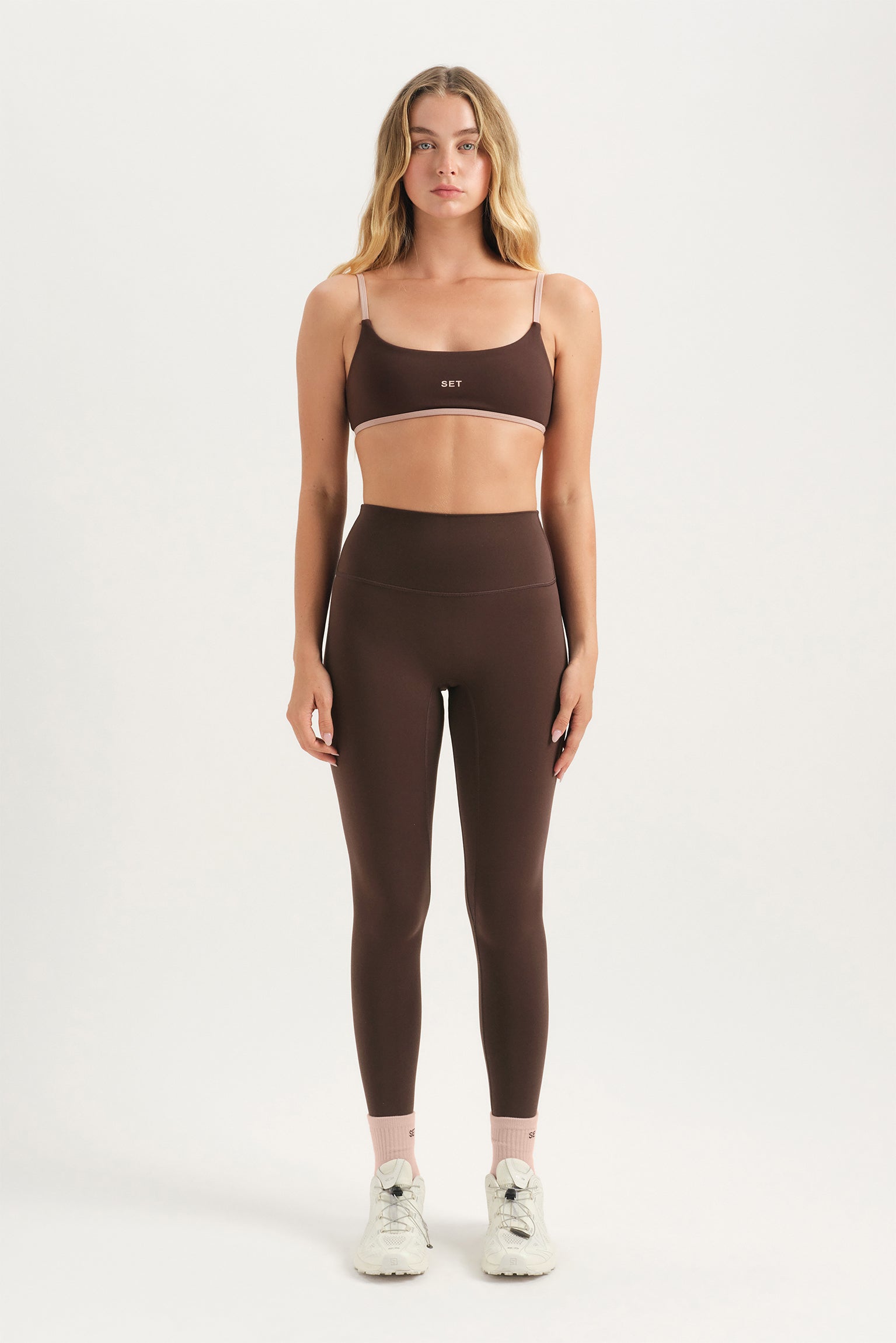 Woman wearing a brown sports bra and leggings set on a white background