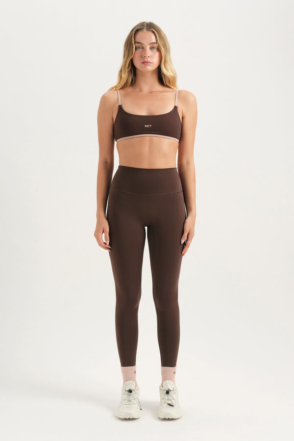 Woman wearing a brown sports bra and leggings set on a white background