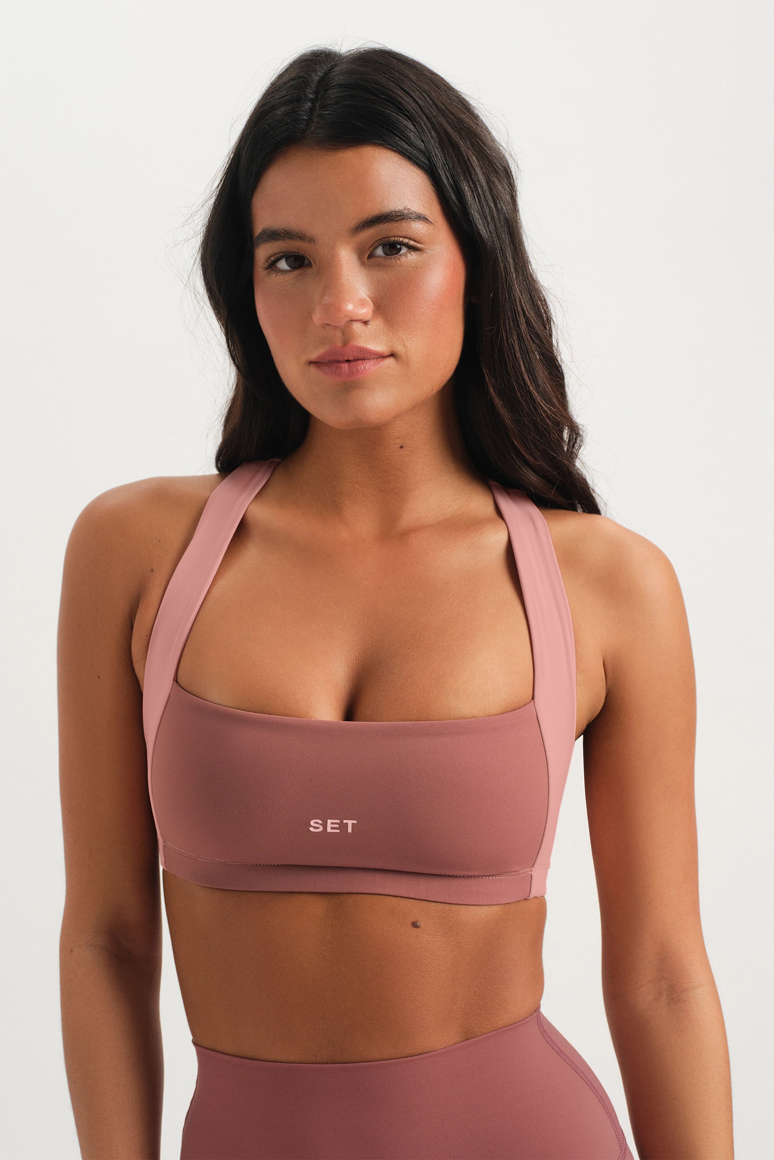 Woman wearing a pink sports bra with 'SET' branding on a white background <model-info>Sydnee wears a size XS and is 5'8", 22” waist, 32BB bust.</model-info>