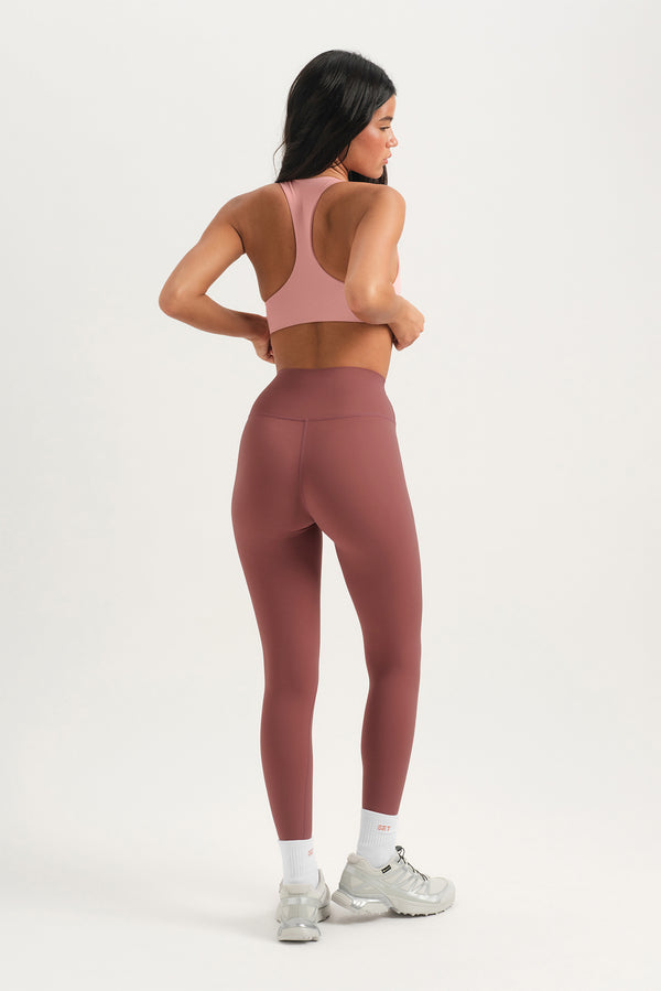 Woman wearing a pink sports bra and leggings on a white background