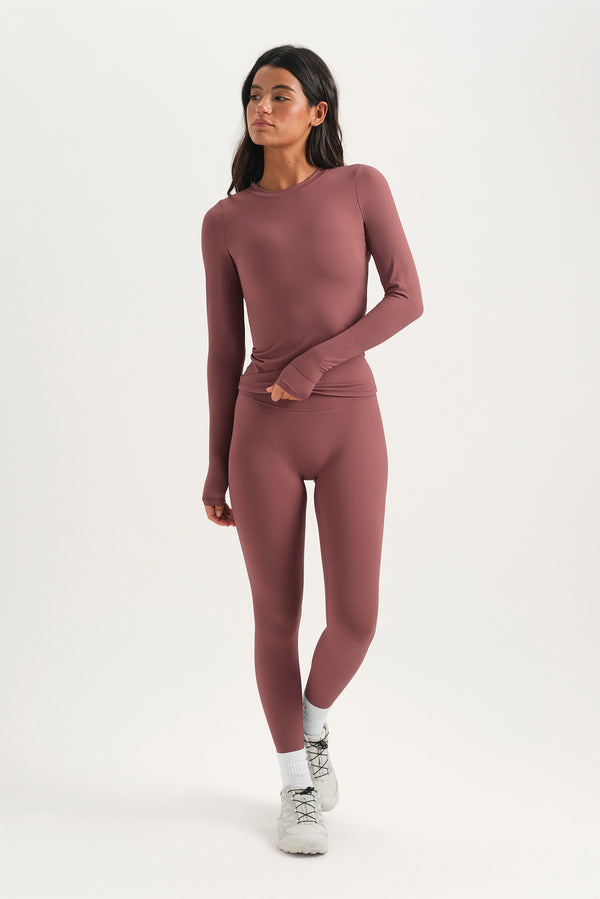Woman wearing a mauve long-sleeve top and leggings set on a white background