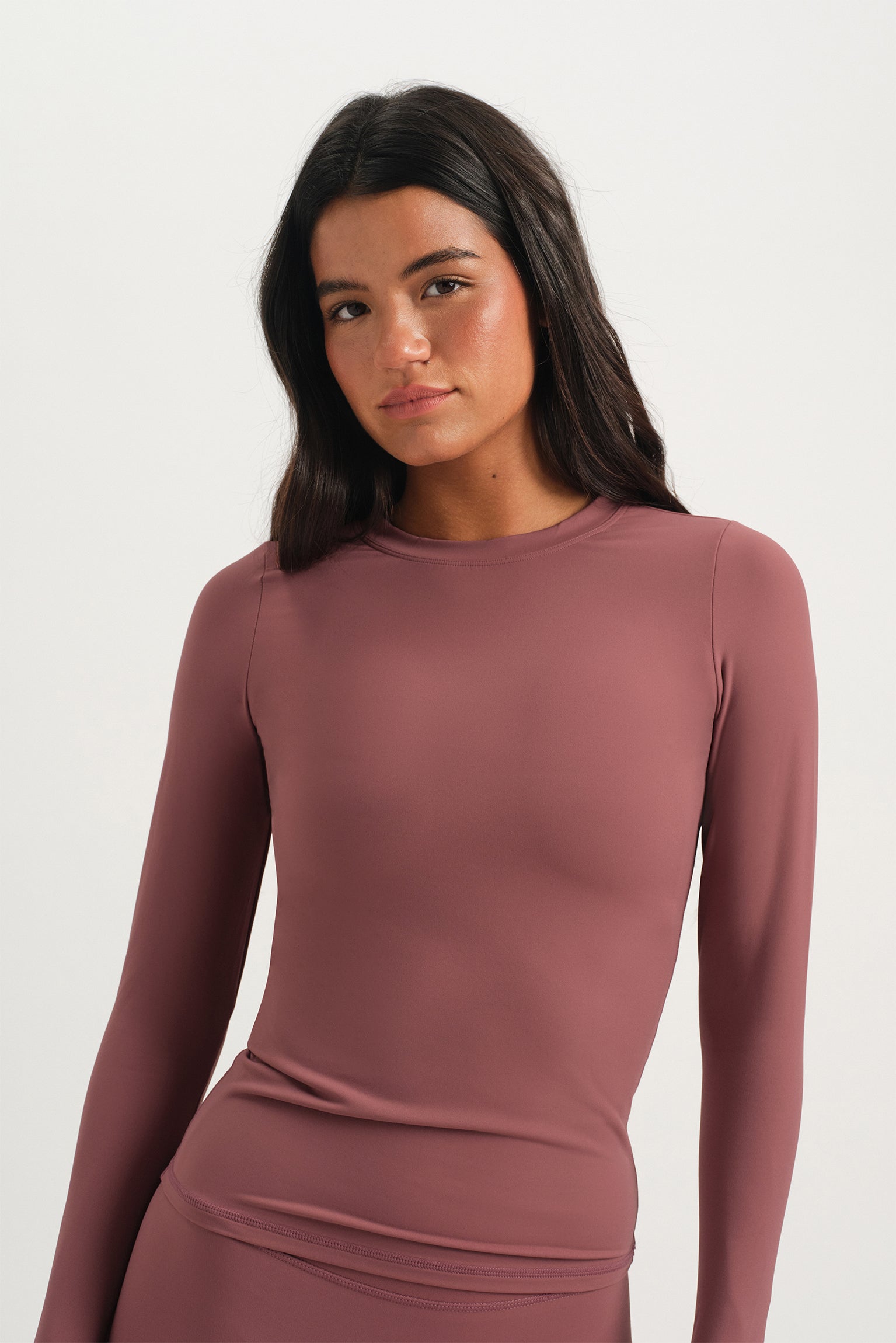Woman wearing a mauve long-sleeve top against a white background 
