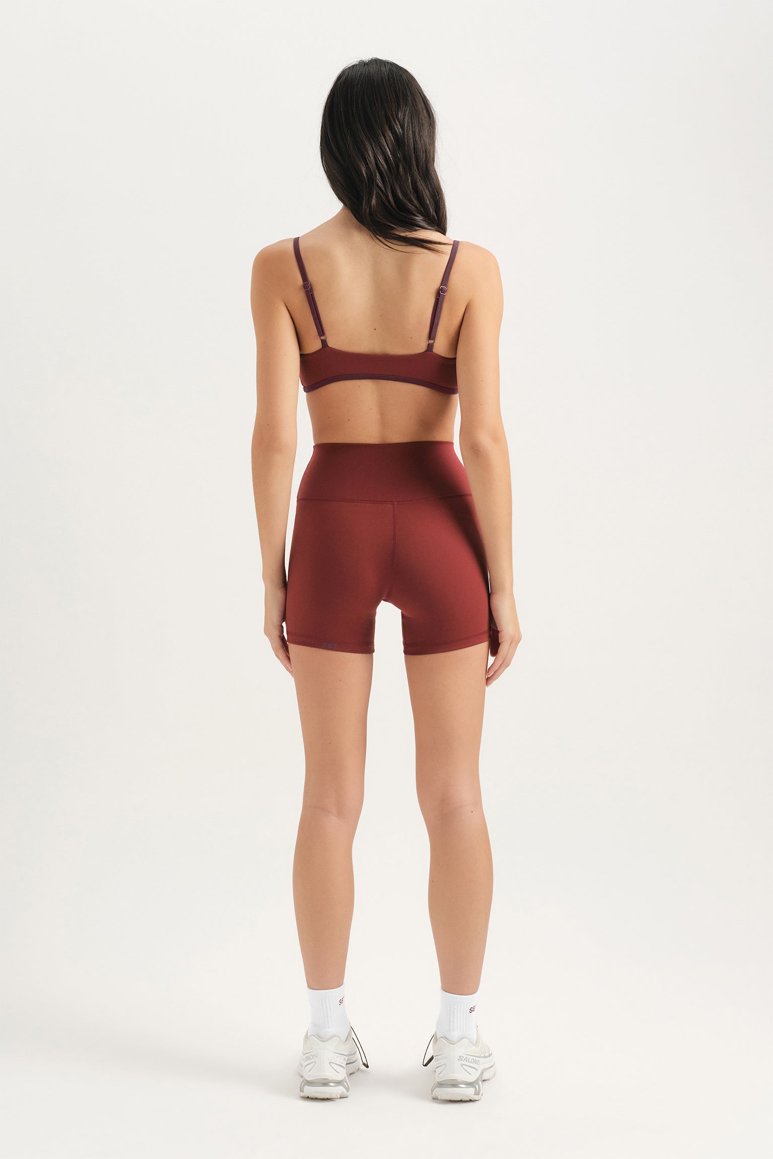 Person wearing a burgundy sports bra and shorts set on a white background