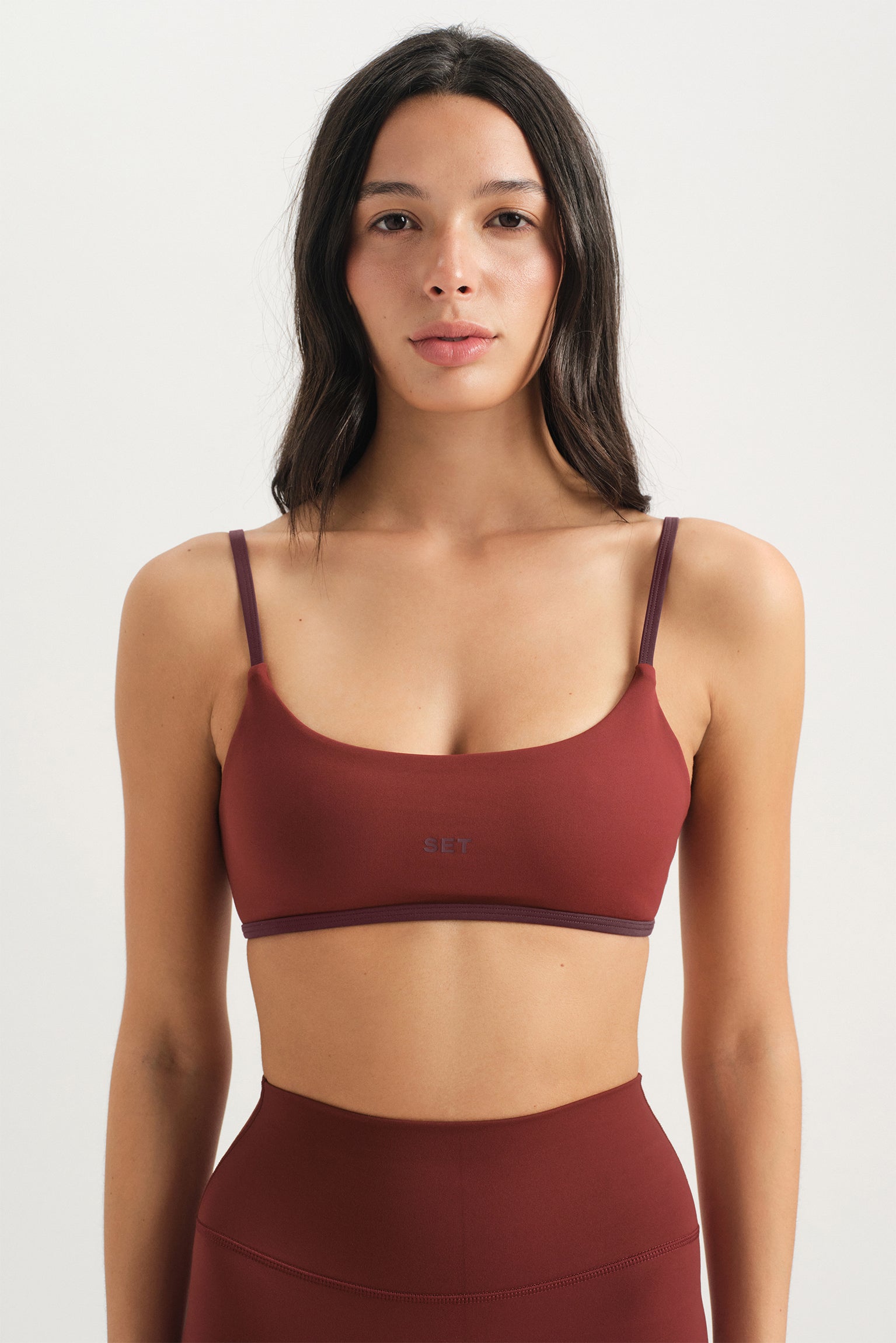 Woman wearing a maroon sports bra and leggings on a white background 