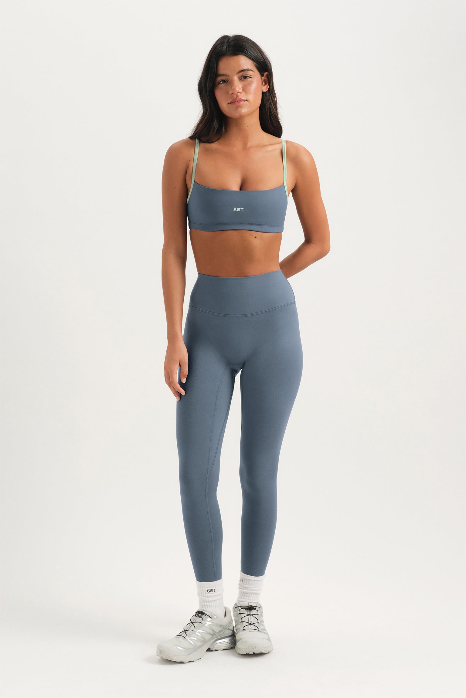 Woman wearing a gray sports bra and leggings set on a white background