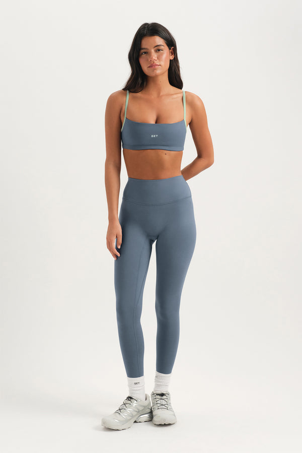 Woman wearing a gray sports bra and leggings set on a white background