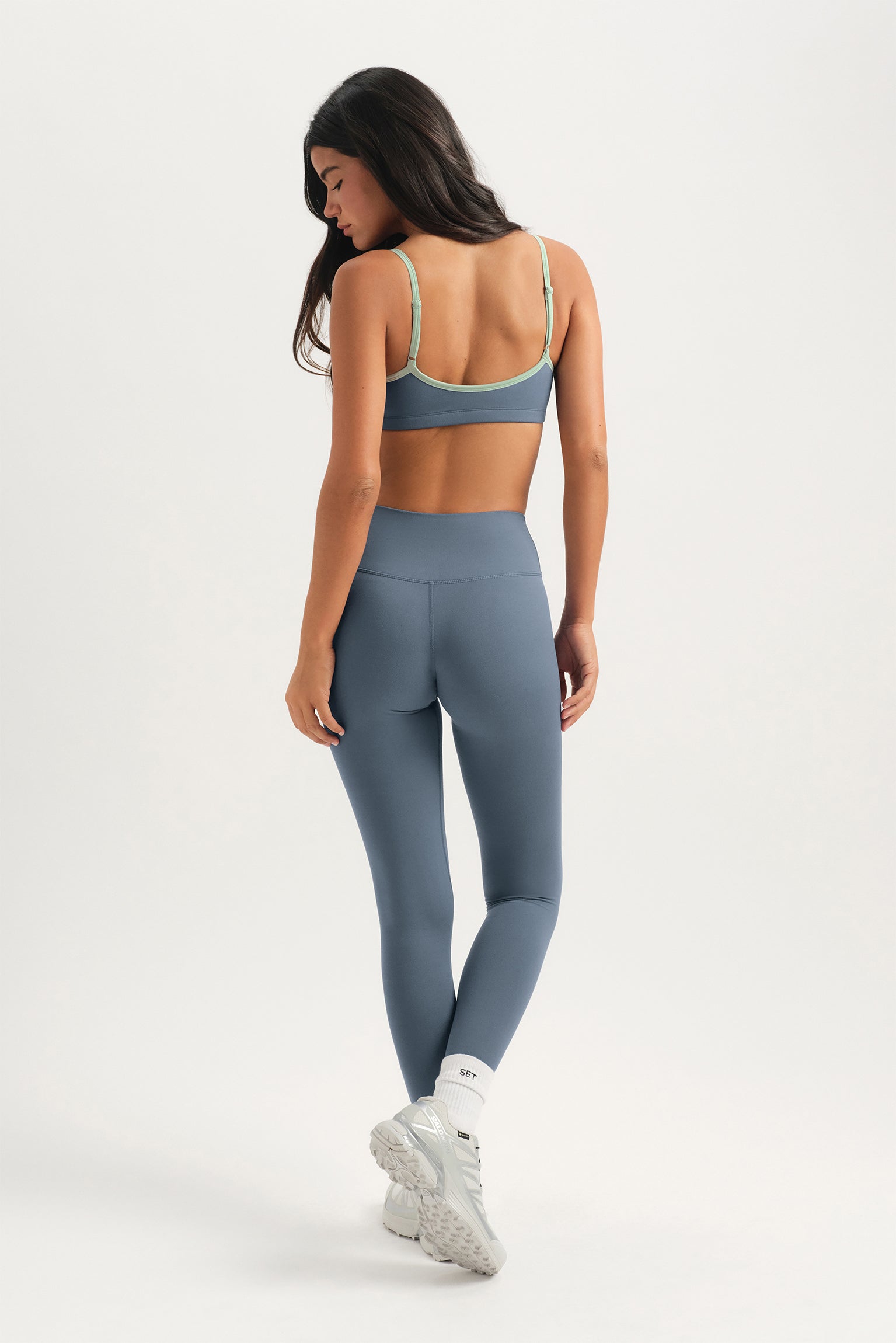 Woman wearing a gray sports bra and leggings on a white background