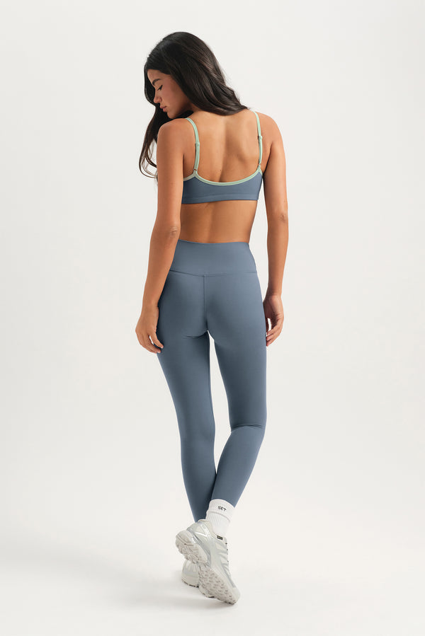 Woman wearing a gray sports bra and leggings on a white background