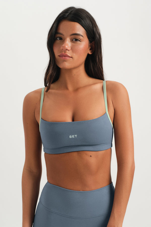 Woman wearing a blue sports bra and leggings with 'SET' branding on a white background 