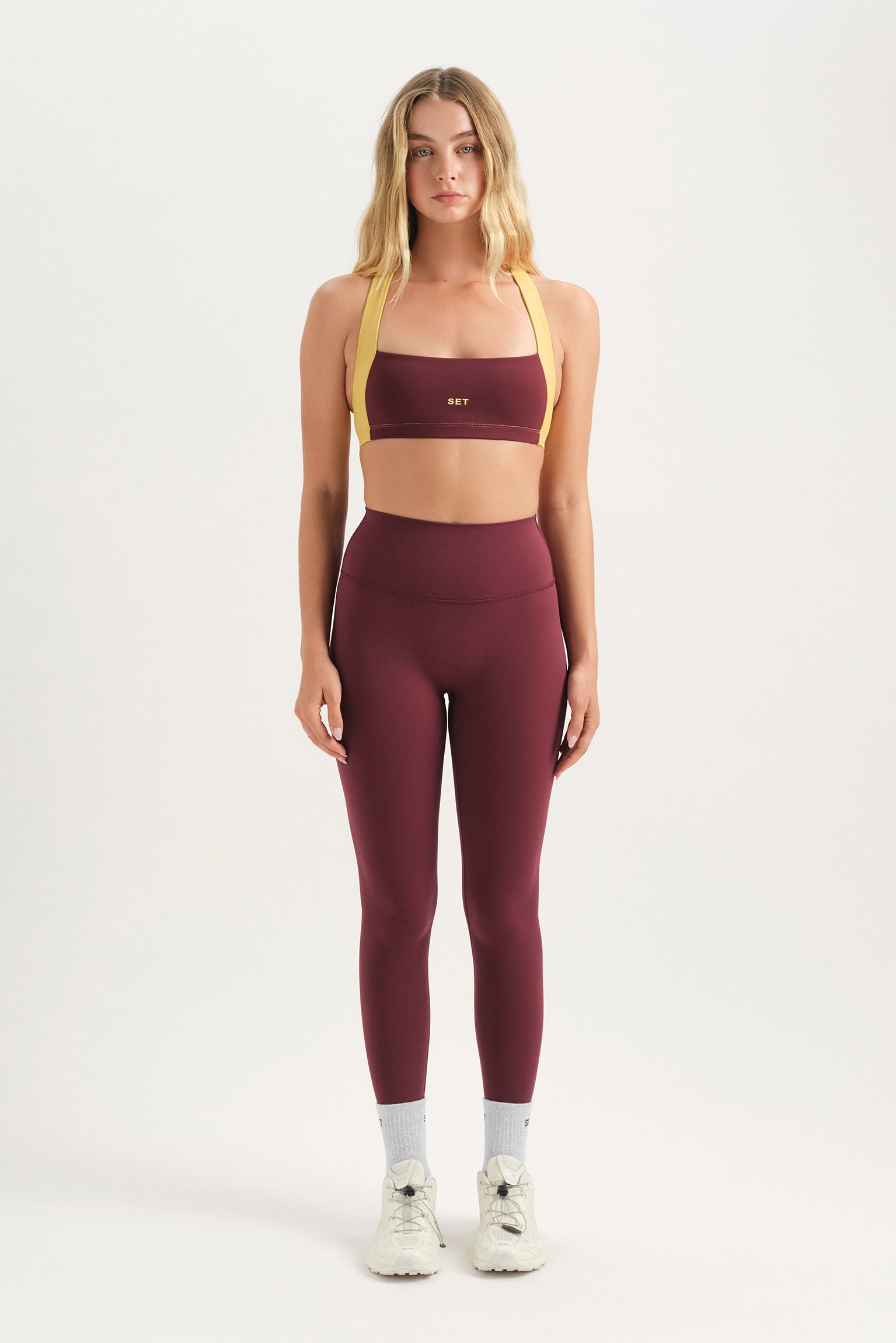 Woman wearing a maroon sports bra and leggings set on a white background
