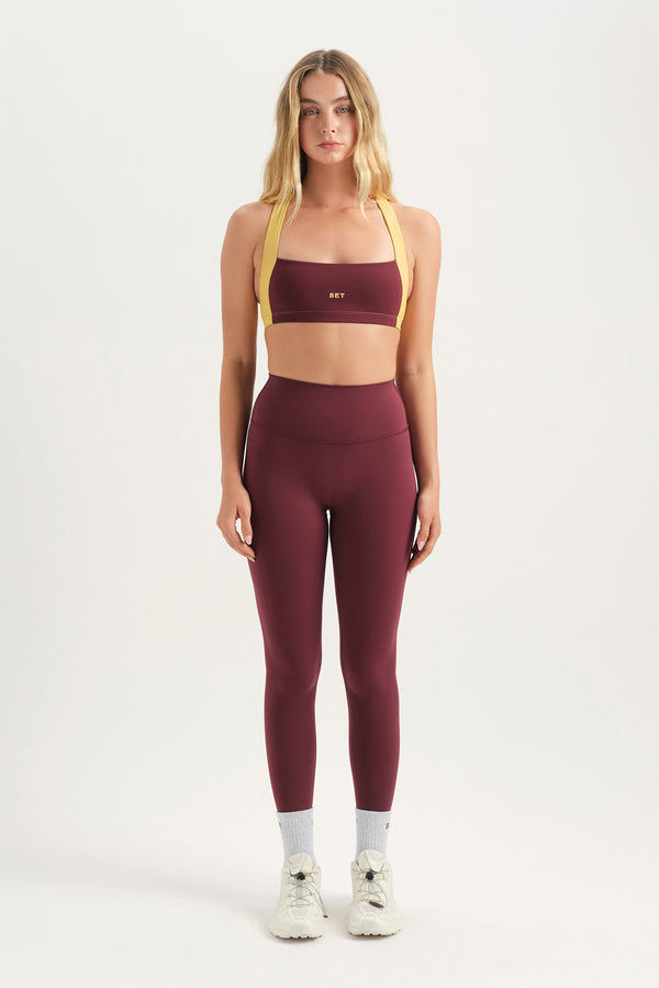 Woman wearing a maroon sports bra and leggings set on a white background