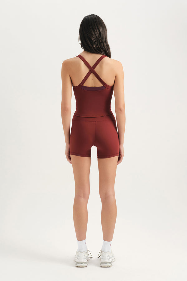 Person wearing a maroon bodysuit with criss-cross straps on a white background